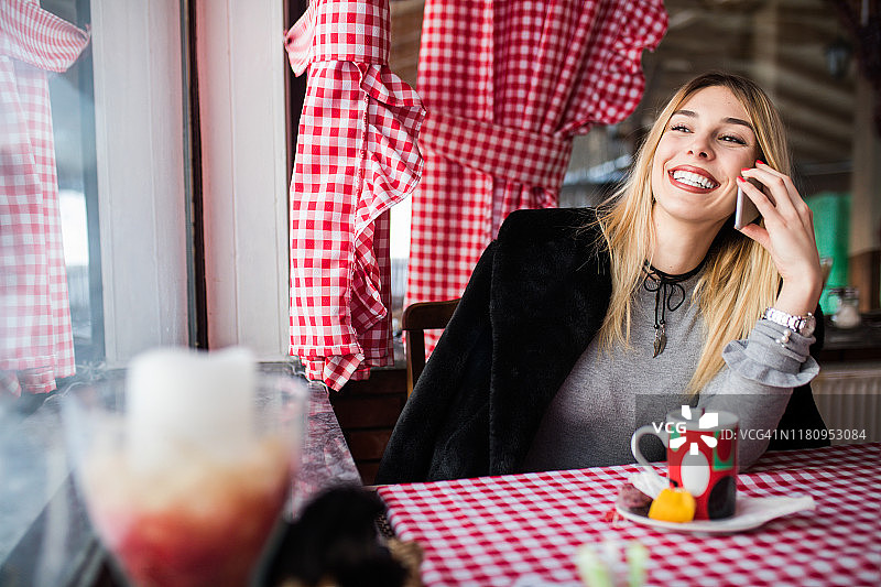 在咖啡馆靠窗边使用手机的可爱女孩图片素材