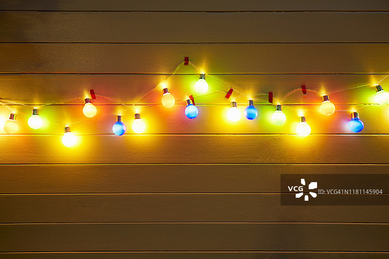 夜晚，黄色木墙上用于派对装饰的彩色灯串图片素材