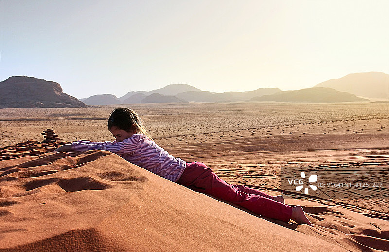在约旦瓦迪拉姆沙漠沙丘上坐着的小女孩图片素材