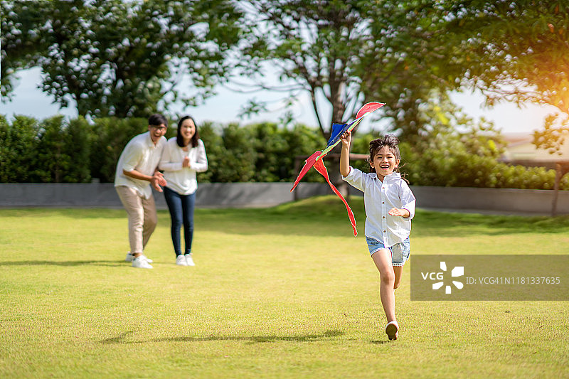 亚洲女儿奔向父母，在乡村公园和家人一起玩风筝，亲子和童年生活图片素材