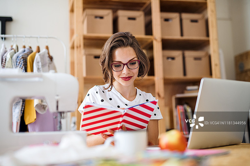 年轻创意女性在室内用笔记本电脑改造旧衣服图片素材