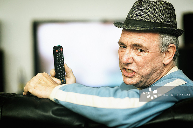 戴着帽子的愤怒老年男人拿着电视遥控器图片素材