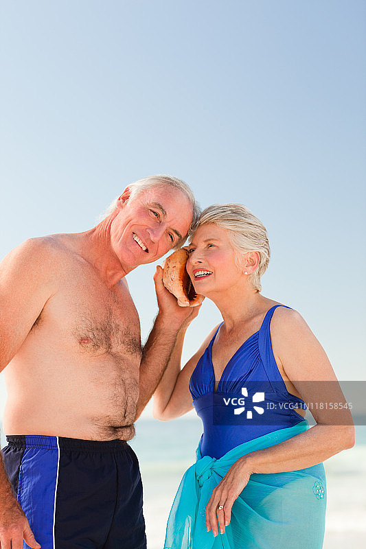 退休夫妇倾听海螺的声音图片素材