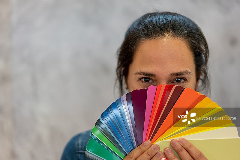 拿着色卡，眼神俏皮地看着镜头的漂亮女人图片素材