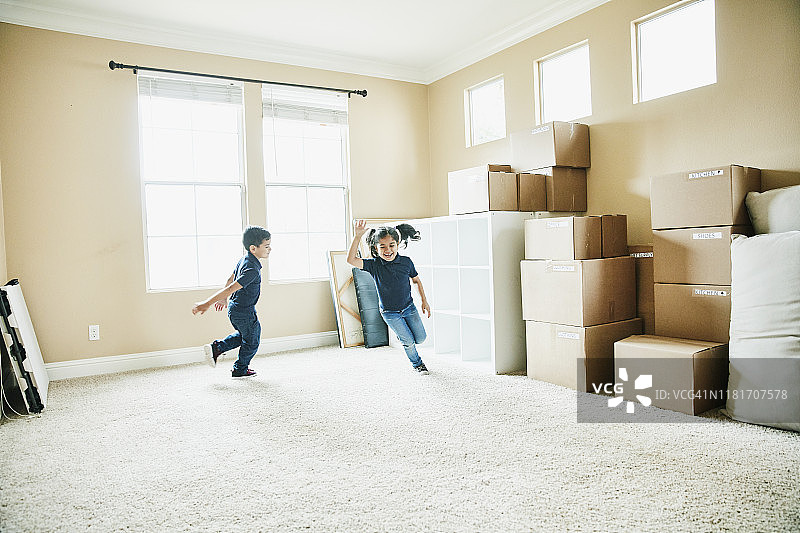 搬家日，年轻的兄妹在堆满纸箱的客厅里奔跑图片素材