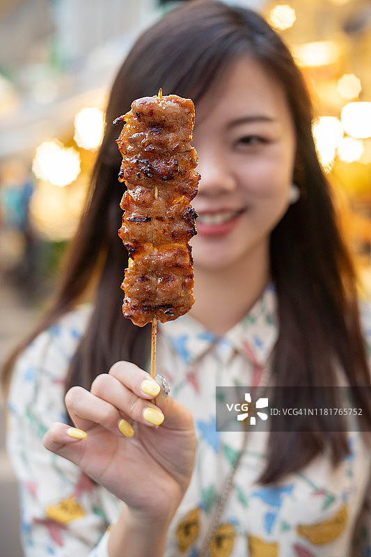 手持从街头小贩处购买的泰式烤猪肉串的亚洲女人图片素材