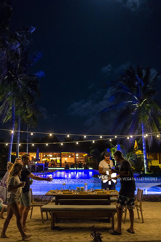 朋友们聚集在热带度假村的灯光下享用晚餐图片素材