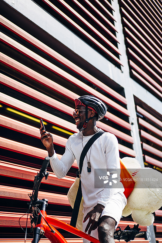 快乐的自行车快递员拿着手机和泰迪熊图片素材