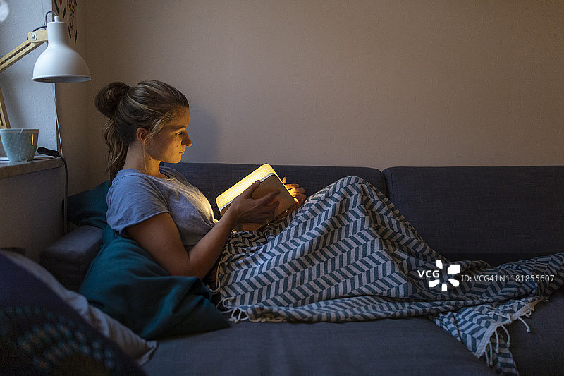年轻女人在家中沙发上阅读发光书图片素材