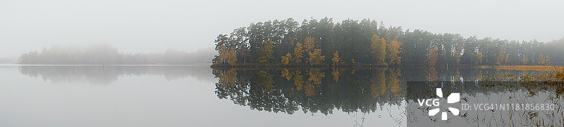 秋日薄雾中森林背景的静谧湖泊全景图片素材