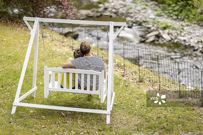 坐在花园秋千上微笑的人的后视图图片素材