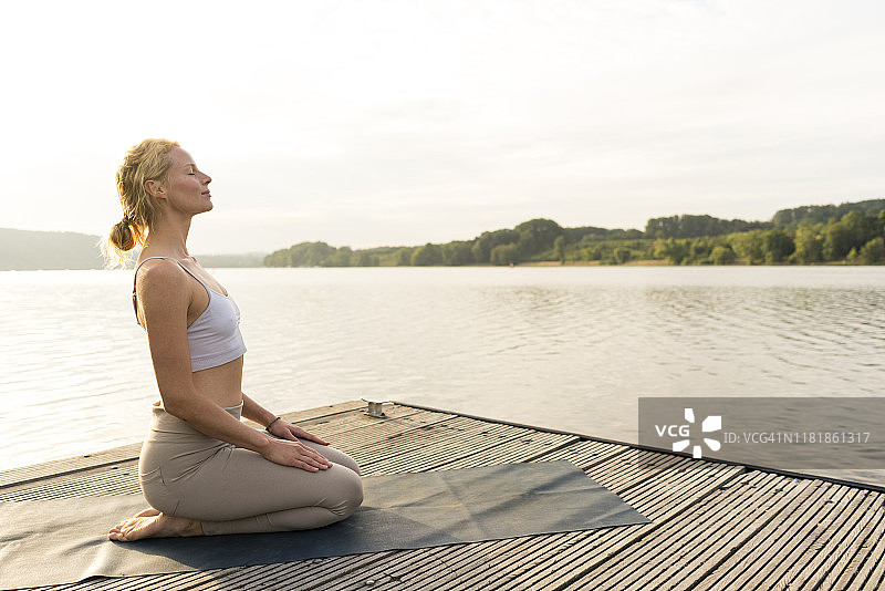 年轻女人在湖边码头上练习瑜伽图片素材