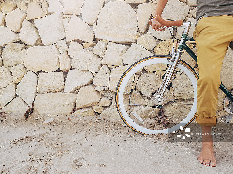 赤脚男人在海滩天然石墙前骑死飞自行车（局部）图片素材