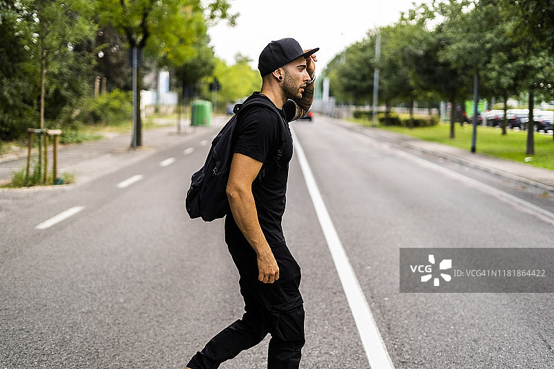 年轻男子背着背包穿过城市街道图片素材