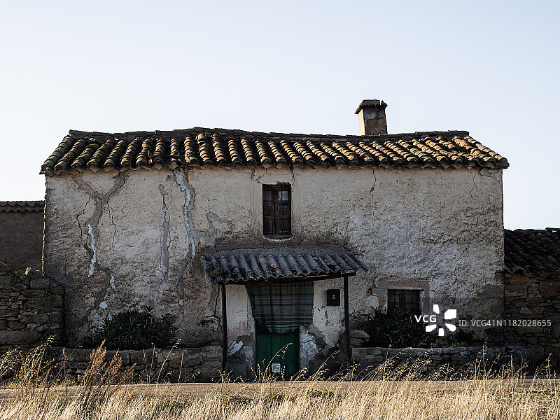 萨拉曼卡省（西班牙）的废弃房屋废墟，木门上挂着破窗帘，信箱，窗户玻璃破碎，外墙有大裂缝，乡村人口减少概念图片素材