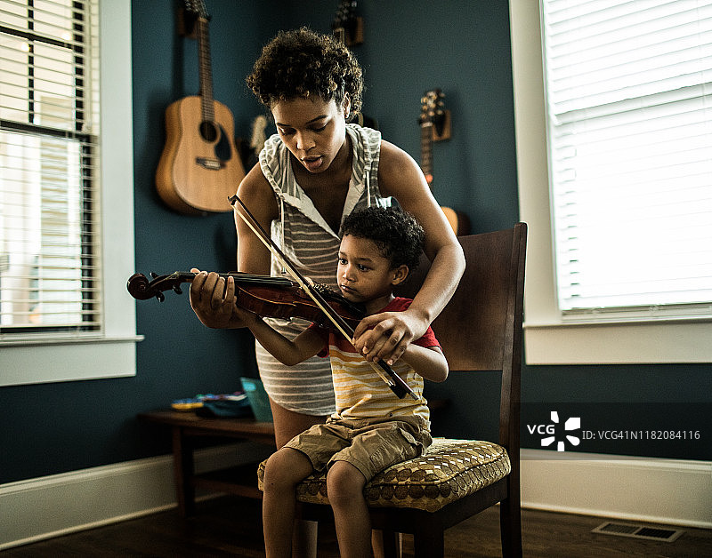 母亲帮助小男孩（3岁）练习小提琴图片素材