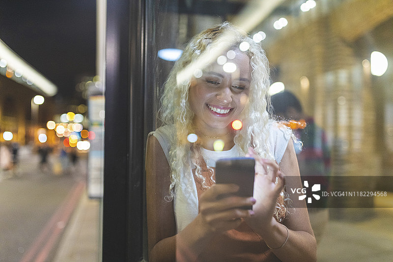 在伦敦夜晚看智能手机等公共汽车的年轻女人图片素材