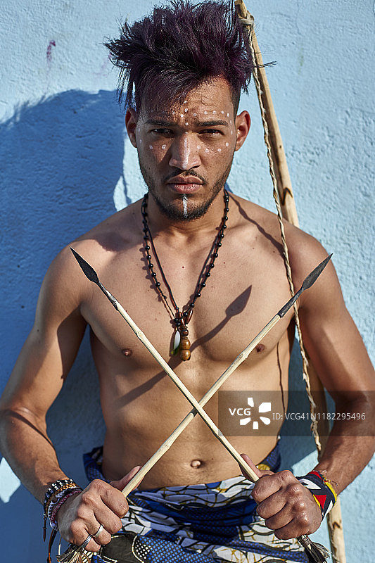 安哥拉卢班戈：依靠在蓝色墙壁上，拿着传统弓箭的部落男子图片素材