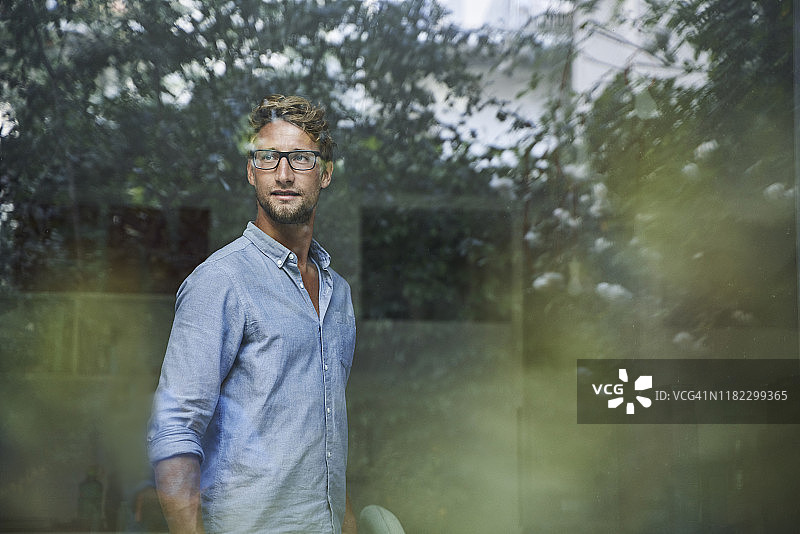 在办公室窗格后面的休闲年轻商人图片素材