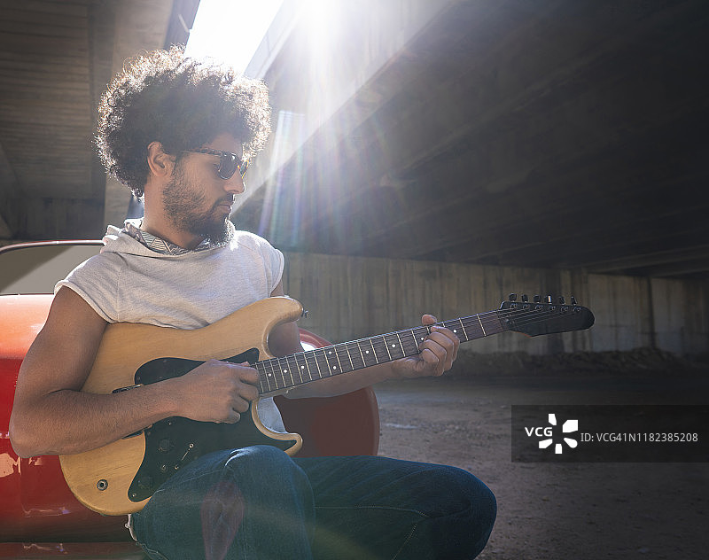 坐在红色汽车上的少数民族年轻吉他手图片素材