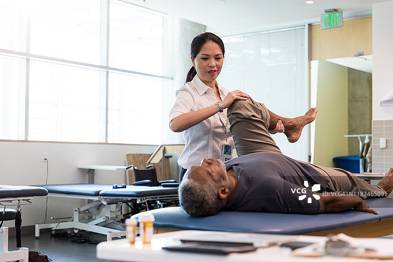 理疗师帮助中年男人弯曲受伤的腿图片素材