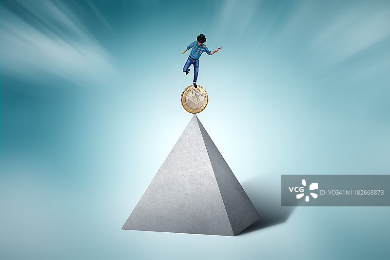 男人在金字塔顶端立着的硬币上保持平衡图片素材