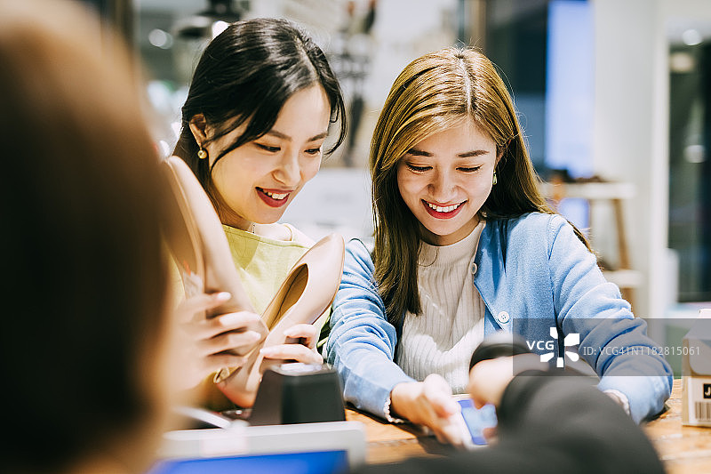 两名亚洲女性在鞋店用智能手机付款图片素材