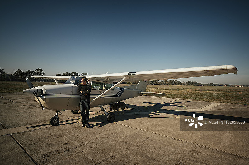男飞行员站在阳光明媚停机坪的小型螺旋桨飞机旁图片素材