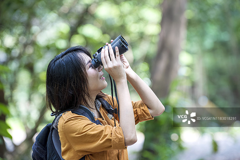 快乐的亚洲年轻女性用双筒望远镜观鸟，自然爱好者概念图片素材