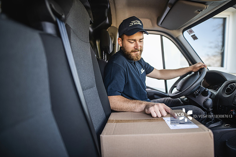 正在仔细检查包裹地址的年轻胡须送货司机图片素材