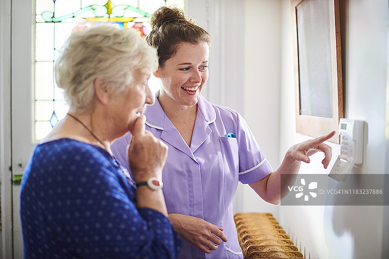 家庭护理员向年长女性展示警报面板图片素材