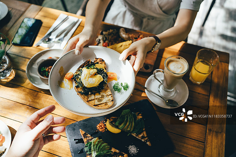 高角度拍摄：户外餐厅早午餐，女子向朋友传递食物图片素材