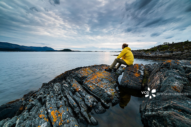 身穿黄色夹克的旅行者在峡湾欣赏日落，挪威图片素材