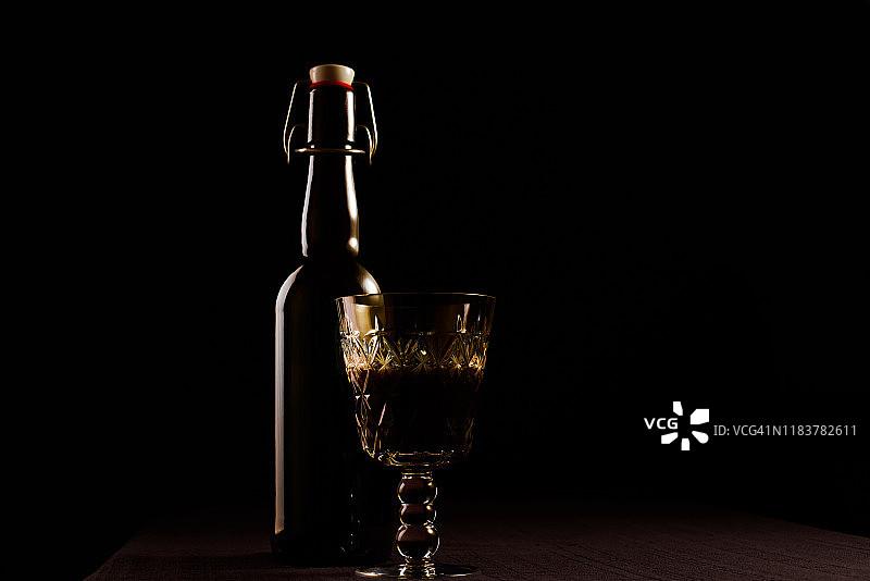 桌子上放着一瓶葡萄酒和一个水晶玻璃杯。深色背景图片素材