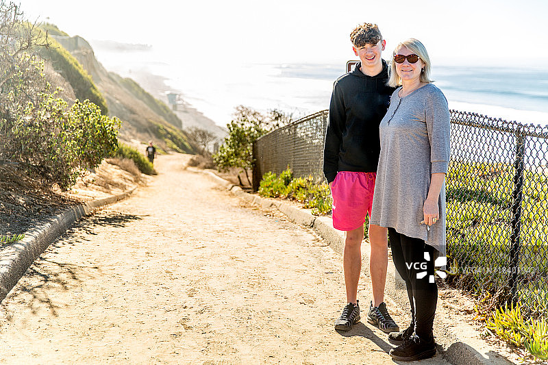 母亲和青少年儿子走在通往大海的走道上图片素材