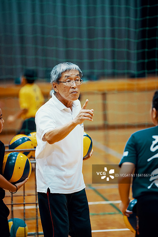 在排球队训练中，年长的男教练向年轻女孩提供建议和指导图片素材