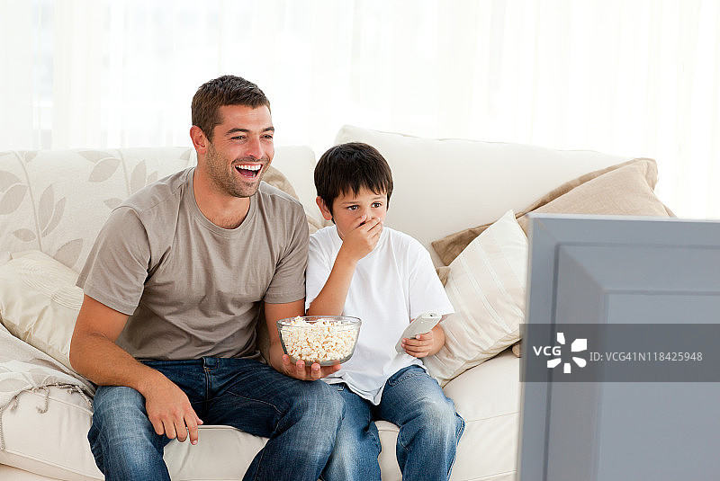 快乐的男人和儿子一起坐在沙发上看电视图片素材