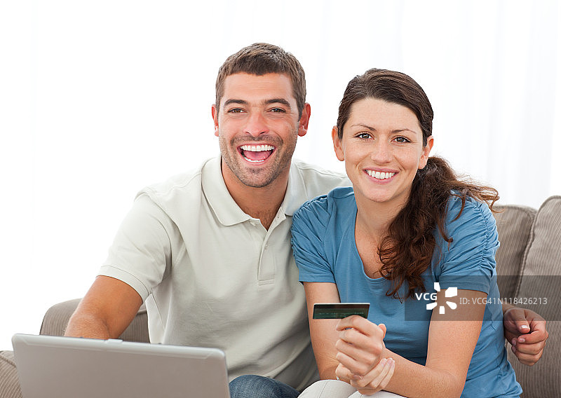 可爱的夫妇坐在客厅里，手持笔记本电脑和信用卡图片素材