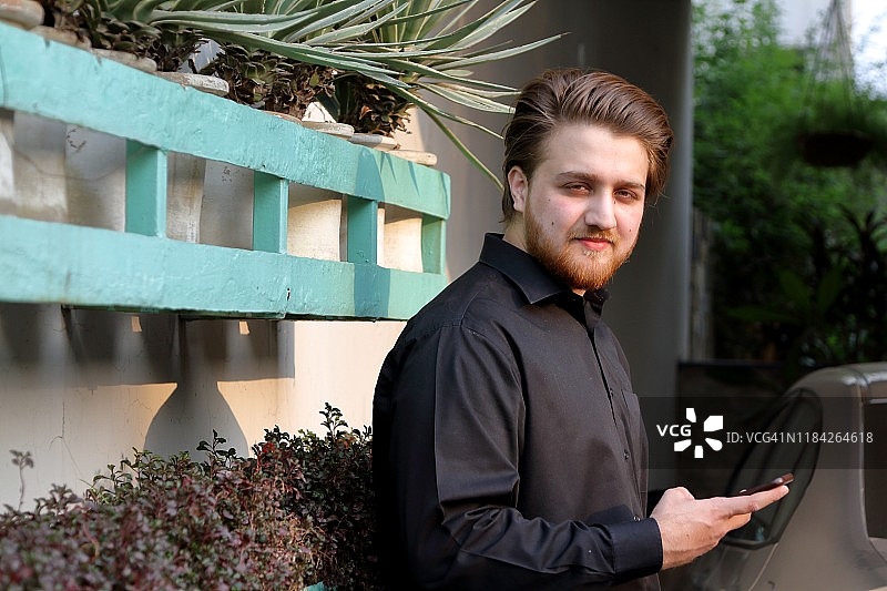 一位年轻的亚洲成年男子正在使用手机并看着镜头图片素材