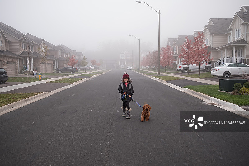 女孩在雾蒙蒙的郊区道路中间遛狗，全身像图片素材