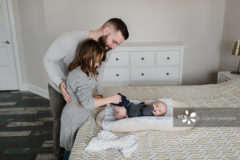女孩和父亲在床上给弟弟换尿布（侧面）图片素材