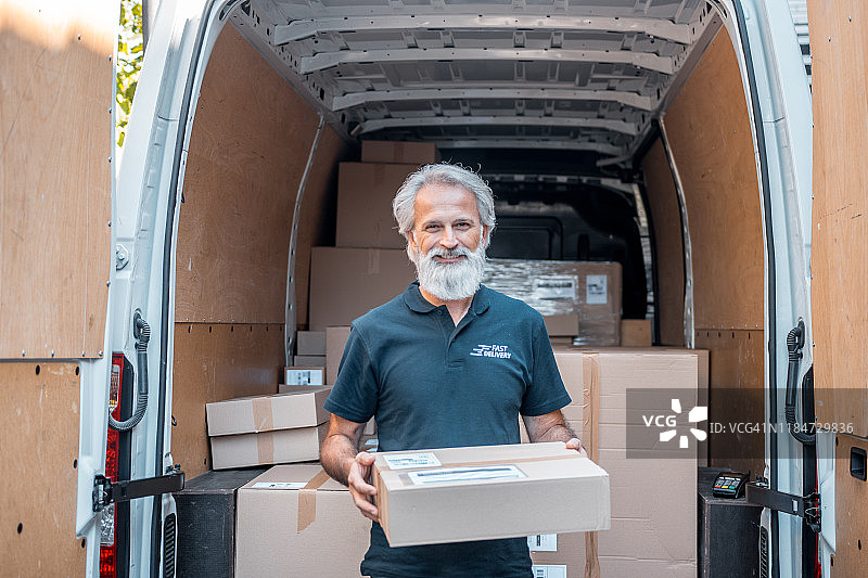 在送货车前拿着包裹微笑的老年男人肖像图片素材