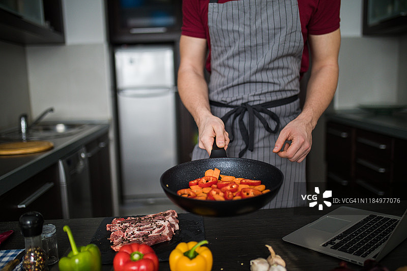 用平底锅烹饪蔬菜的年轻男人图片素材