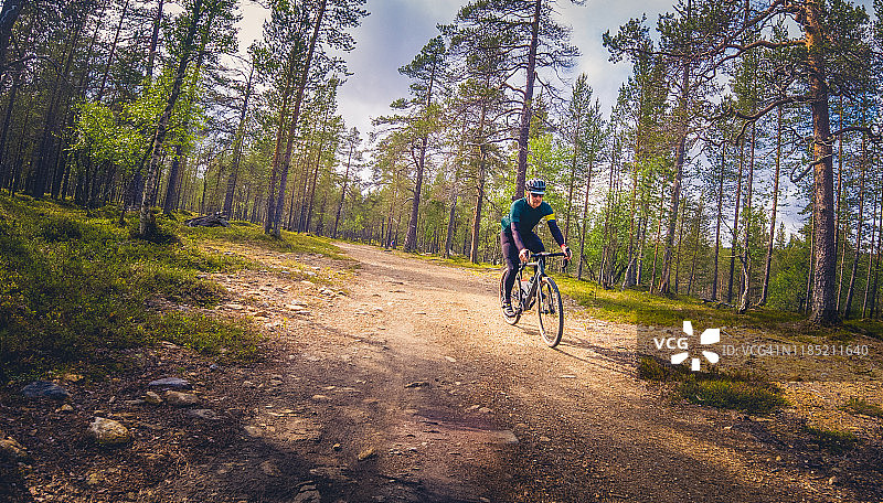 在芬兰拉普兰，骑自行车的人在狭窄的土路上沿着砂石路下坡图片素材