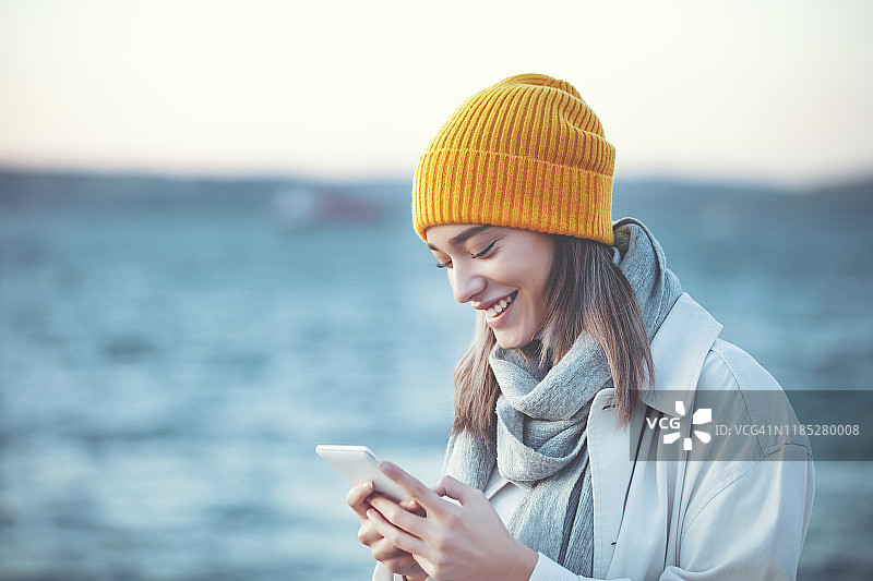 戴黄色帽子的年轻女人在户外使用手机图片素材