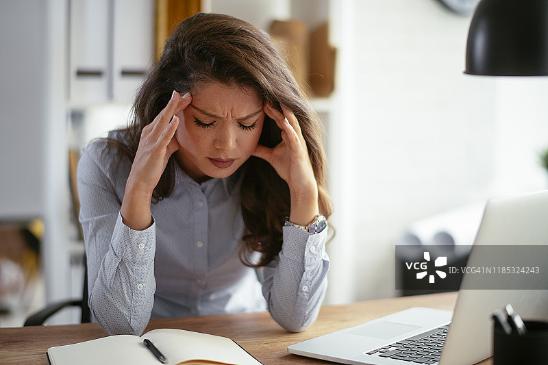 头痛坐在桌子旁的女人。库存照片图片素材