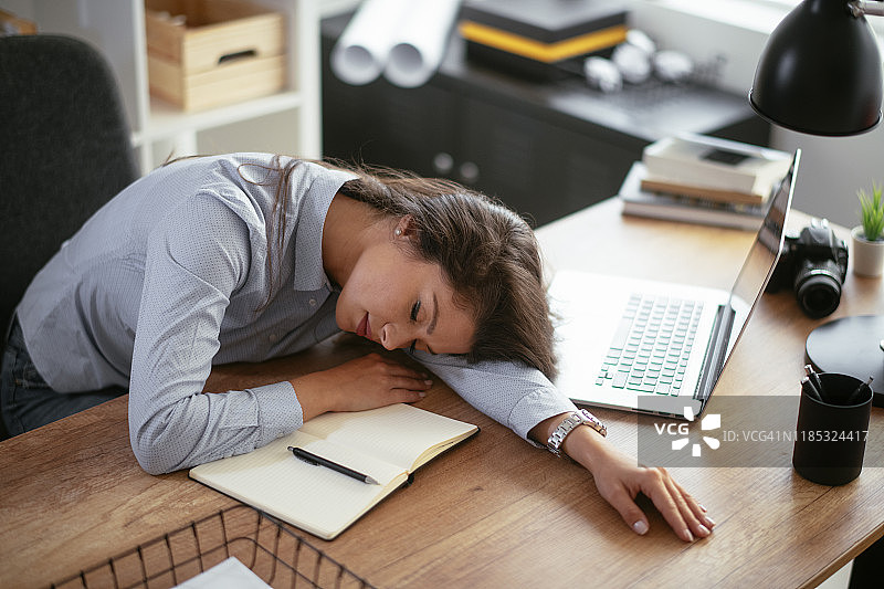 疲惫的女商人趴在办公室桌上小憩图片素材
