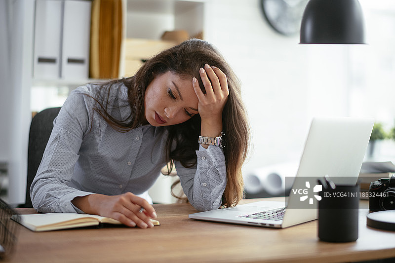 头痛坐在桌子旁的女人。库存照片图片素材