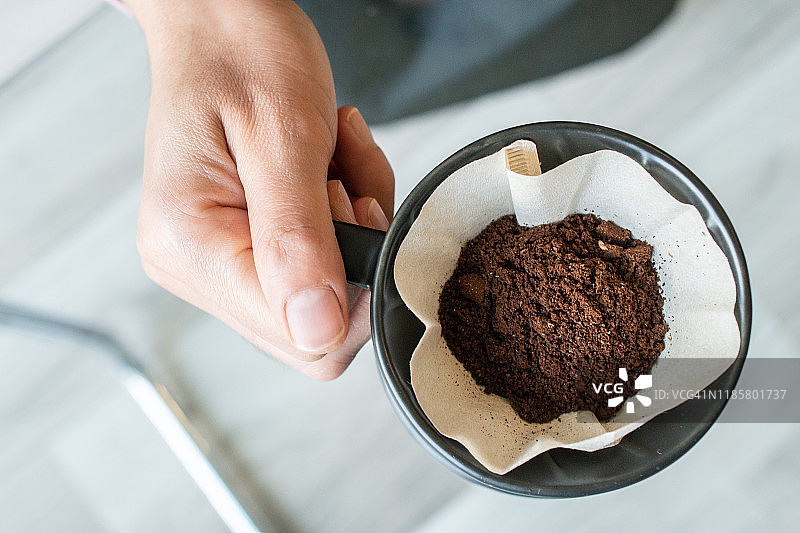 咖啡师手持装有研磨咖啡和滤纸的杯子，准备滴滤的局部视图图片素材