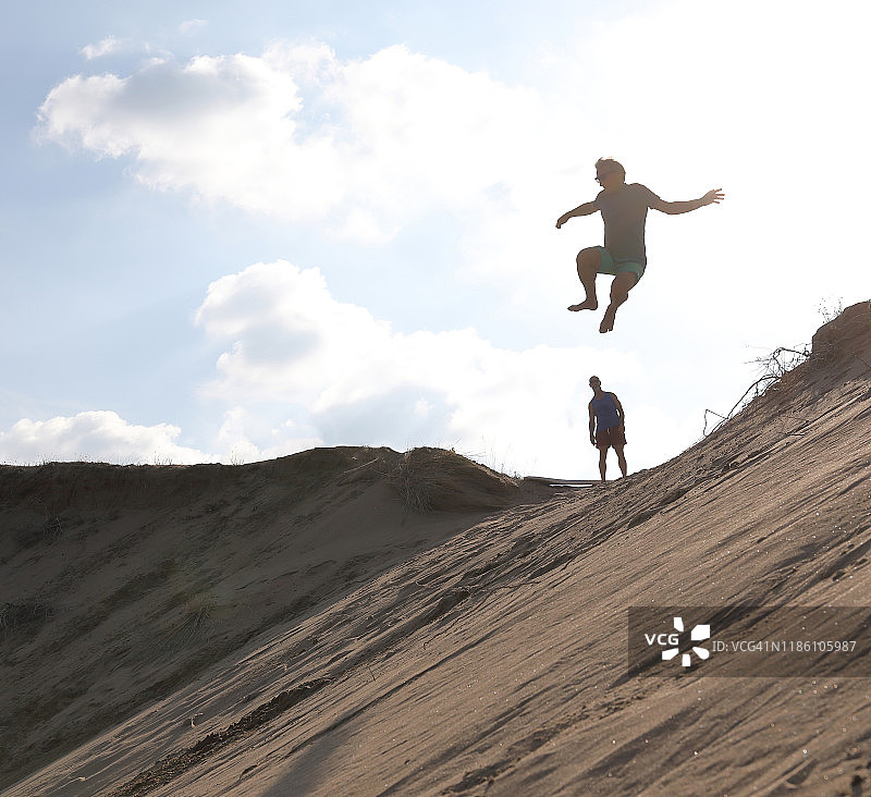 中年男人从沙丘上跳下来，朋友在一旁观看图片素材